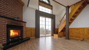 A spacious room with a brick fireplace, wooden flooring, a large window, and a wooden staircase. - Petit Maison Pension (Taean)