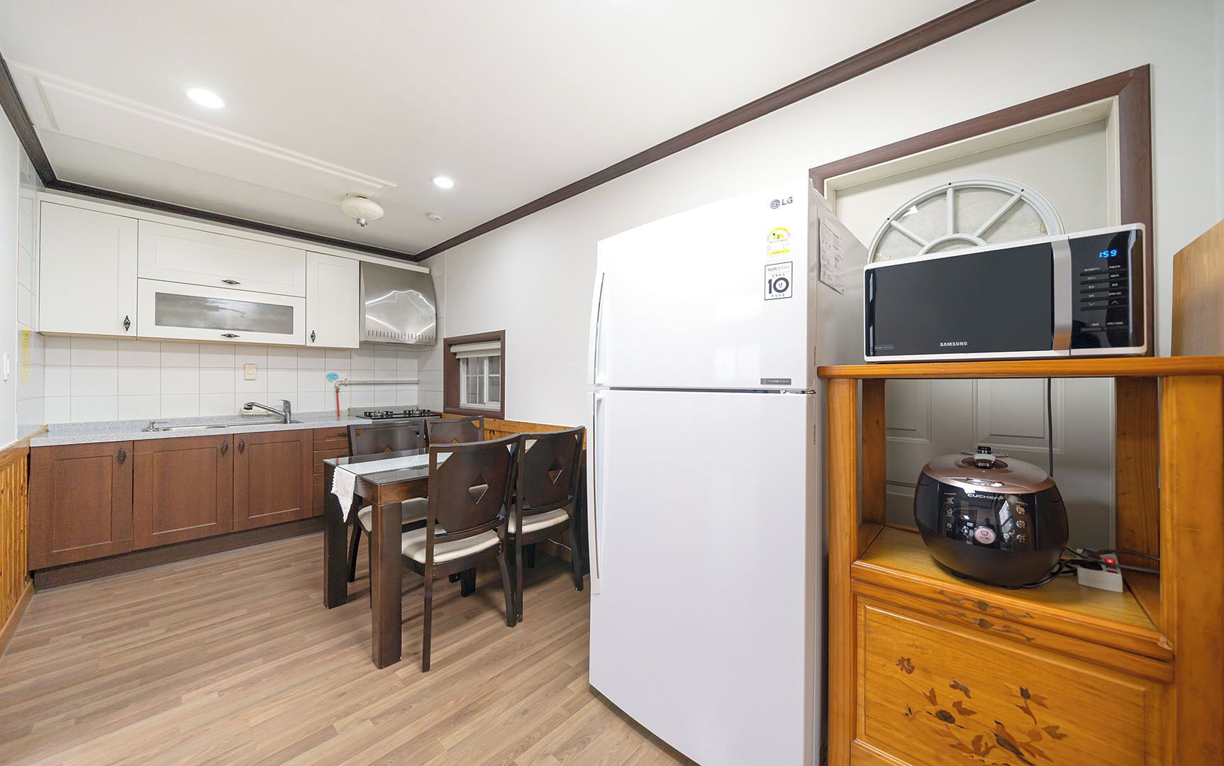 A compact kitchen with white cabinets, a white refrigerator, a microwave, and a wooden cabinet with a decorative item.