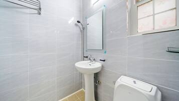 A bathroom with a pedestal sink, a handheld showerhead, a toilet, and a window with a floral view.