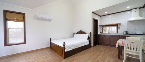 Un dormitorio con cama de madera, una pequeña cocina con lavamanos y armarios, y una ventana con persiana.