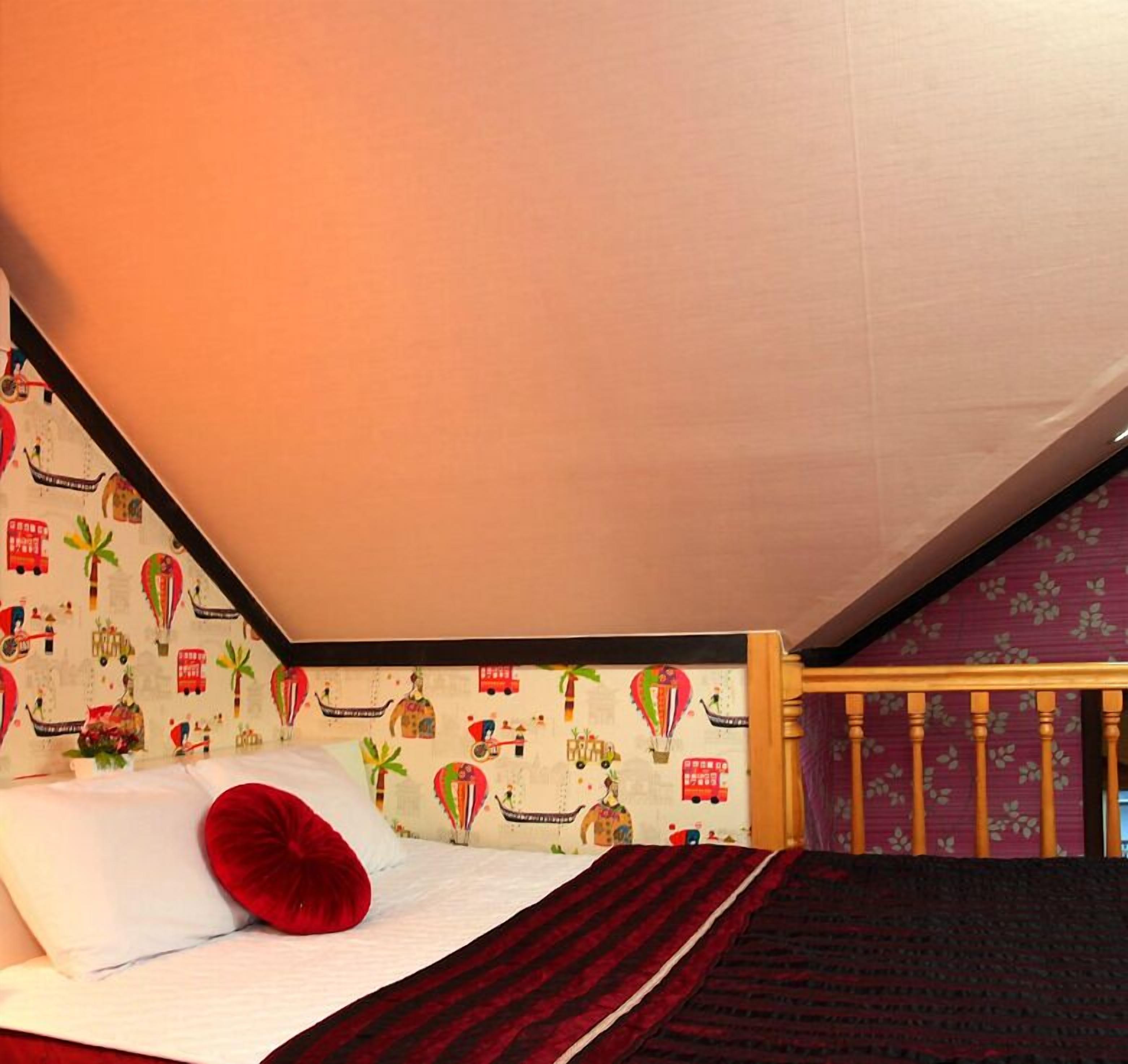 Un dormitorio con cama, almohada roja, pared estampada y cabecera de madera.