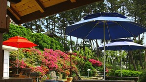 A covered outdoor area with wooden beams, picnic tables, and multiple umbrellas. - Petit Maison Pension (Taean)