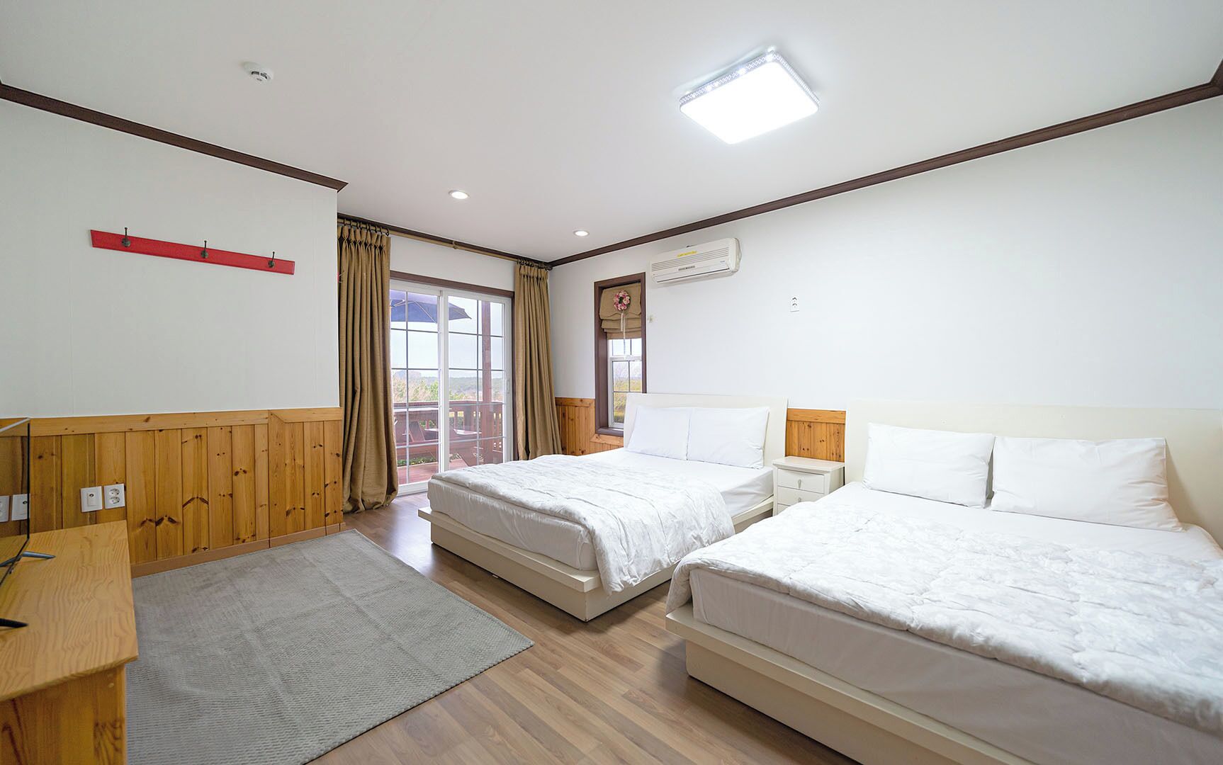 Una camera d'albergo con due letti, una scrivania, una finestra con tende e una lampada a soffitto.