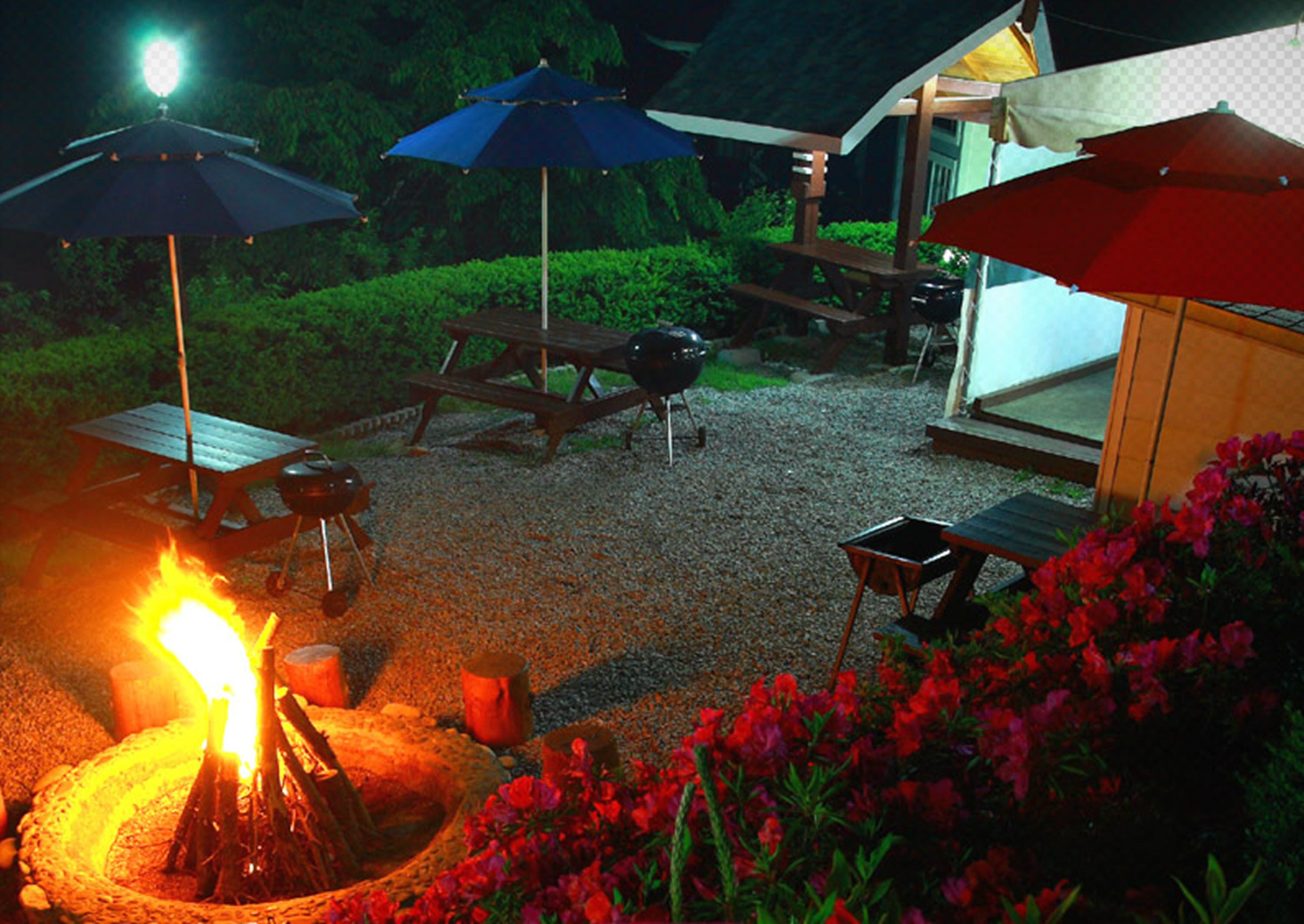 Un patio al aire libre con un pozo de fuego, mesas de picnic y sombrillas.