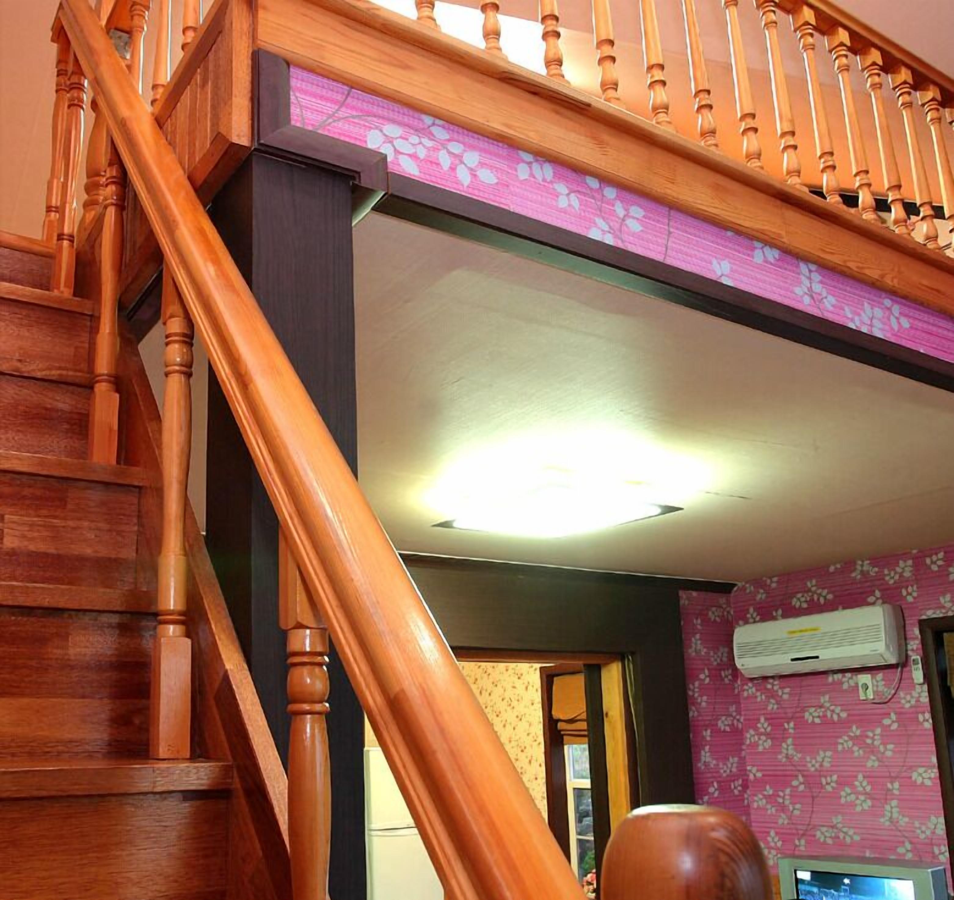 A wooden staircase leading to a room with a pink floral wallpaper and a ceiling light.