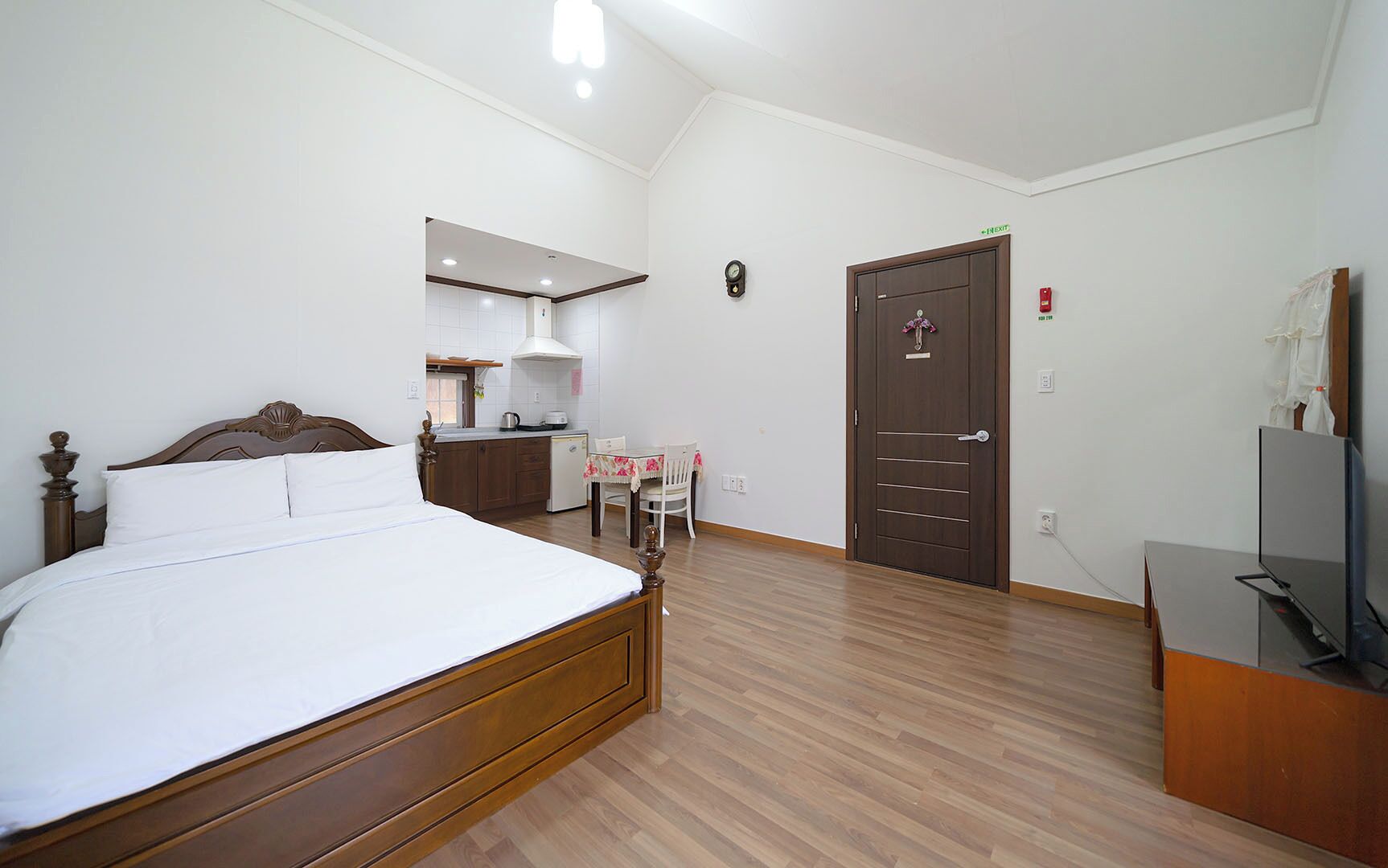 Une chambre avec un lit en bois, une petite kitchenette, une porte et un téléviseur.