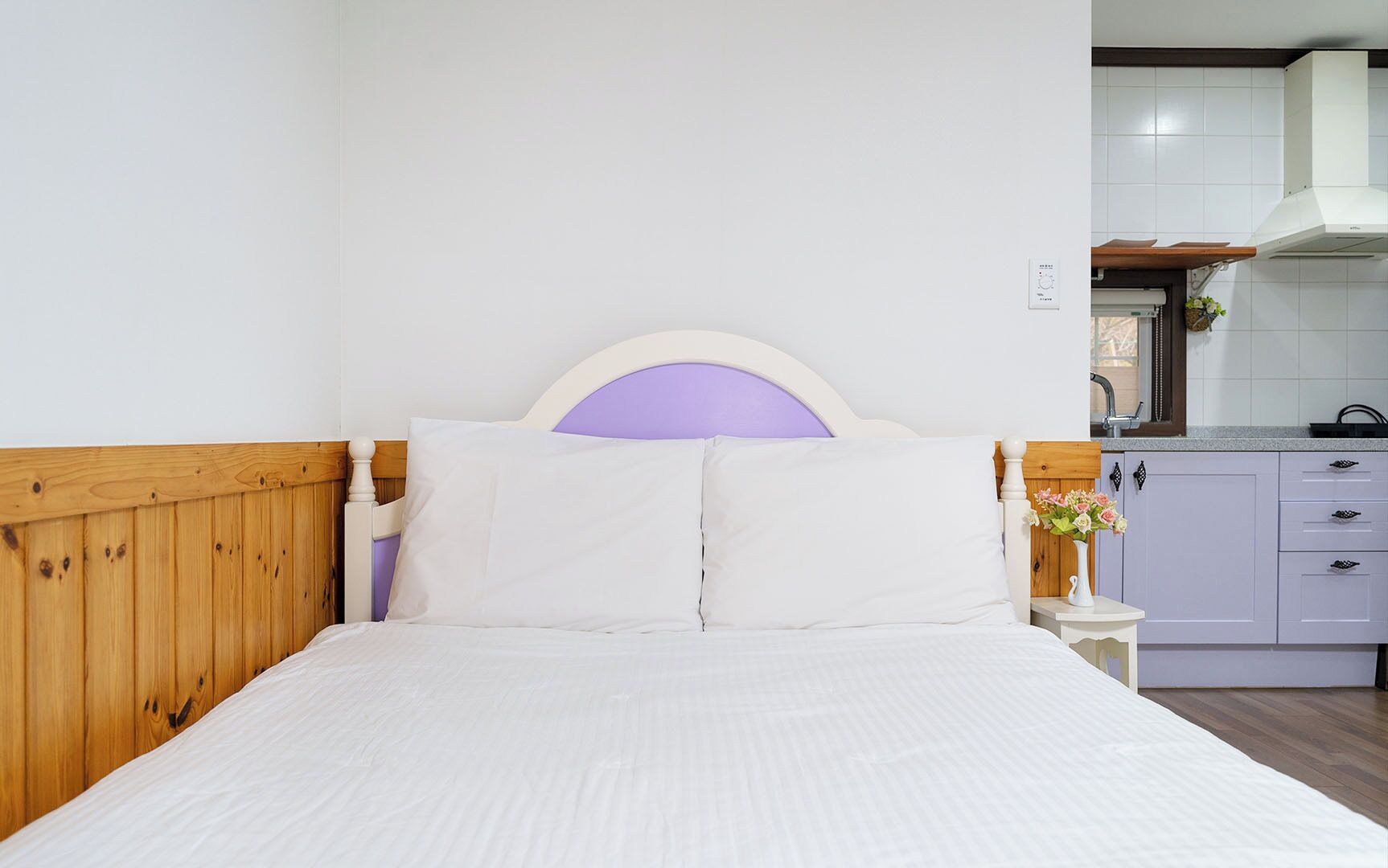 A bedroom with a wooden headboard, white bedding, and a small bedside table with a vase of flowers.