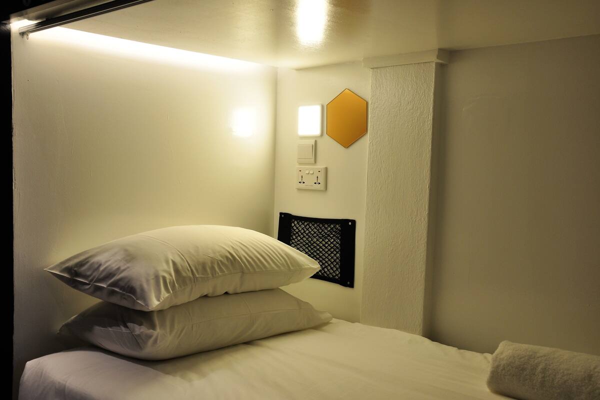 Une chambre d’hôtel équipée d’un lit, d’oreillers, d’un luminaire fixé au mur et d’un thermostat.