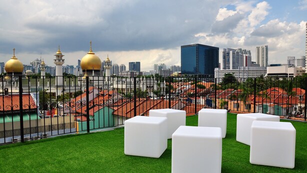A rooftop terrace with white square seating and a view of a cityscape including buildings and a mosque with golden domes.