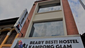 A hostel sign with a colorful bear logo and the text "BEARY BEST! HOSTEL KAMPONG GLAM".