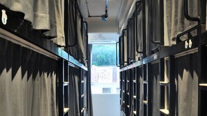 A corridor with lockers and curtains, leading to a window with a view of buildings.