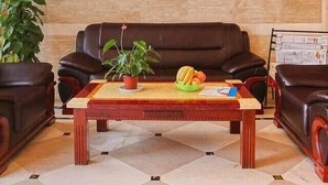 A lobby with a brown leather sofa, a wooden coffee table with fruits, and a large potted plant. - Hangzhou Wangsu Hotel Letong (Hangzhou)