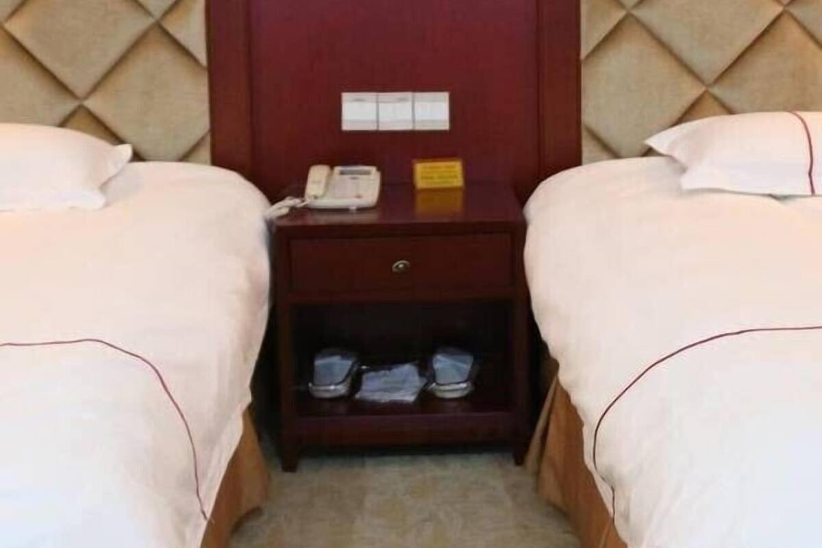 A hotel room with two beds, a nightstand, and a shoe rack.