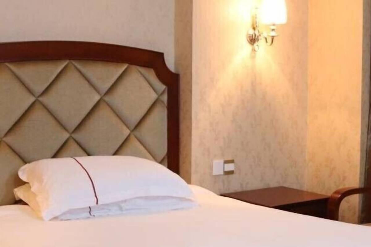 A hotel room with a bed, a nightstand, a wall-mounted lamp, and a chair.