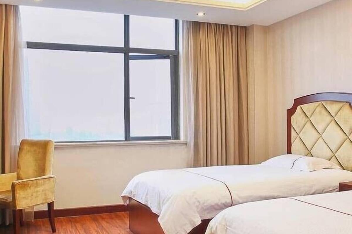 A hotel room with two beds, a chair, a large window, and wooden flooring.