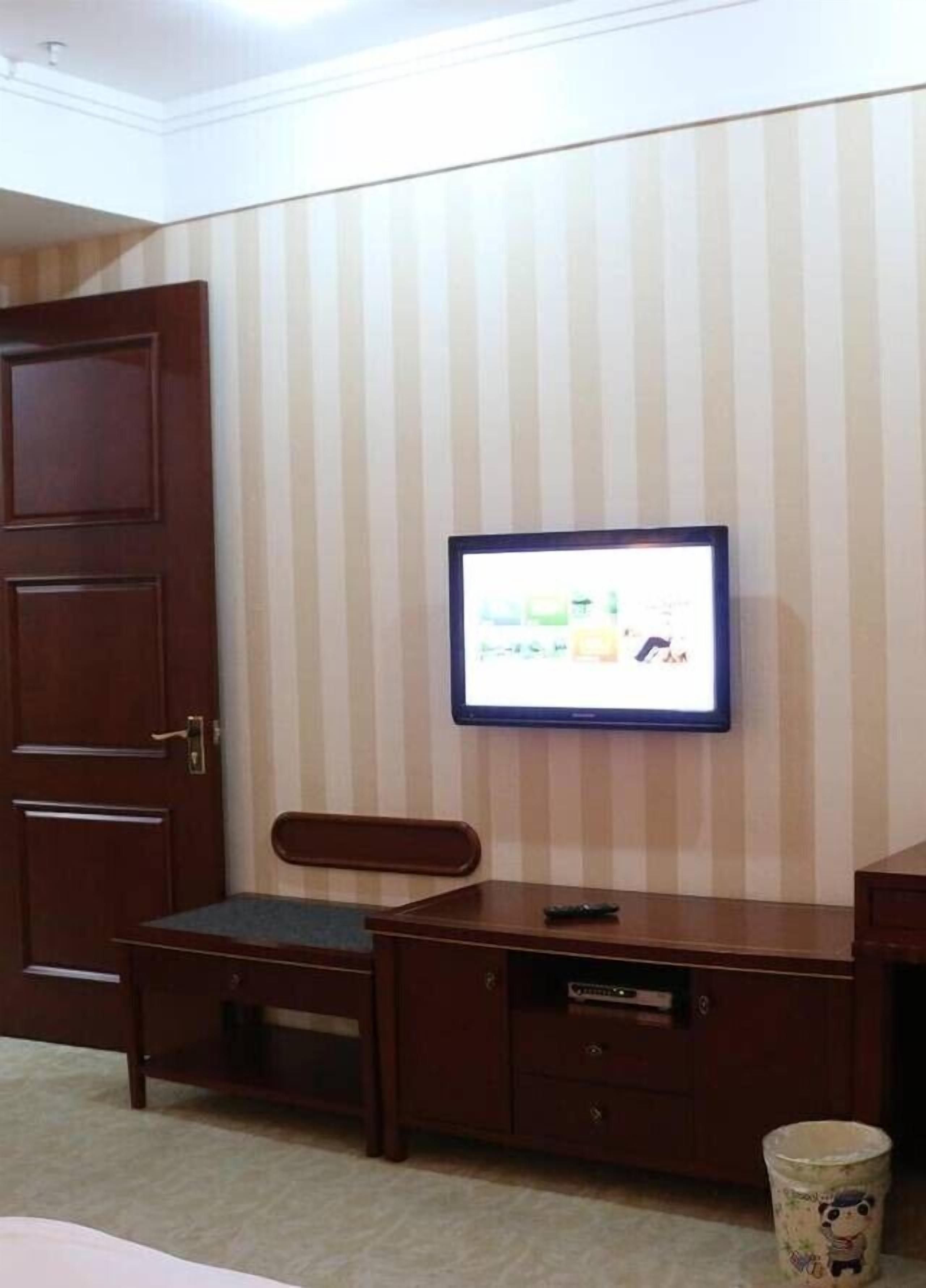 Een hotelkamer met een aan de muur bevestigde televisie, een houten bureau, een stoel en een kleine afvalbak.