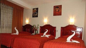 A hotel room with three beds, each with a red bedspread and a swan-shaped pillow. There are two wall-mounted lamps, a painting on the wall, and a wooden headboard. - inkayra hotel (Cusco)
