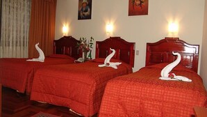 A hotel room with two beds, each with a wooden headboard and red bedding. There are wall-mounted lights and two paintings above the beds. - inkayra hotel (Cusco)