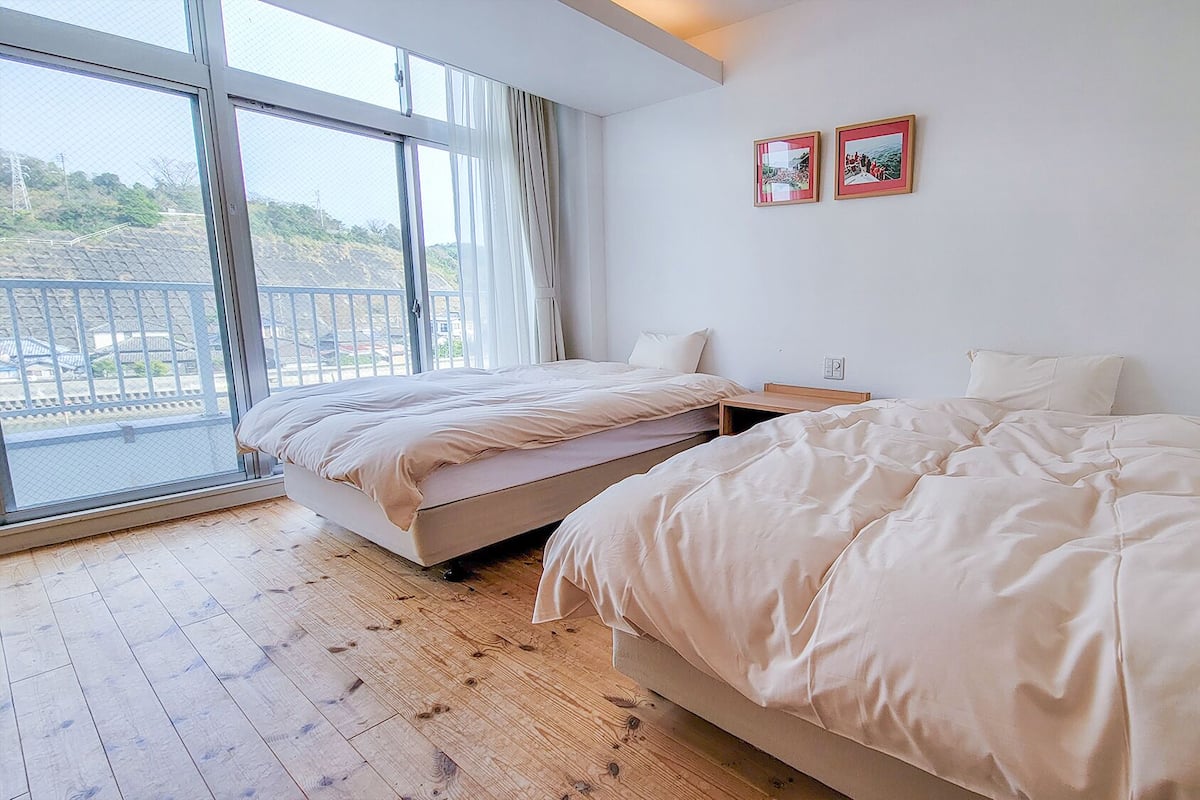 Une chambre avec deux lits, une grande fenêtre et deux tableaux encadrés accrochés au mur.