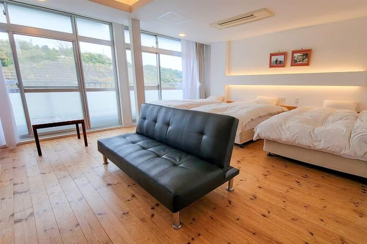 Une chambre d’hôtel moderne, dotée d’un canapé, de deux lits, de grandes fenêtres et offrant une vue sur l’extérieur.