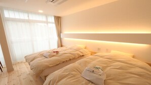 Quarto de hotel com duas camas, uma janela grande com cortinas translúcidas e uma cabeceira moderna com iluminação integrada.