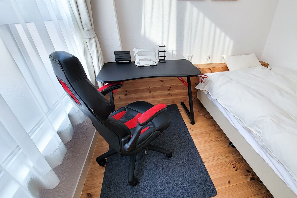 Une petite pièce bien rangée, avec un lit, un bureau et une chaise, et une fenêtre avec des rideaux.