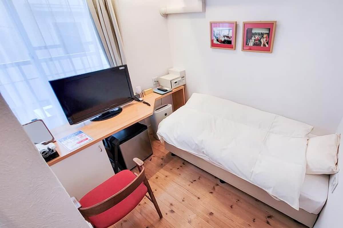 Une petite chambre avec un lit simple, un bureau, une chaise, un téléviseur et deux tableaux encadrés accrochés au mur.