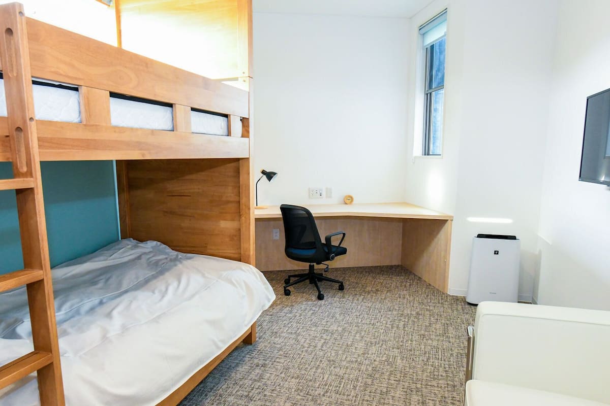 Une chambre avec un lit superposé, un bureau, une chaise et un téléviseur.