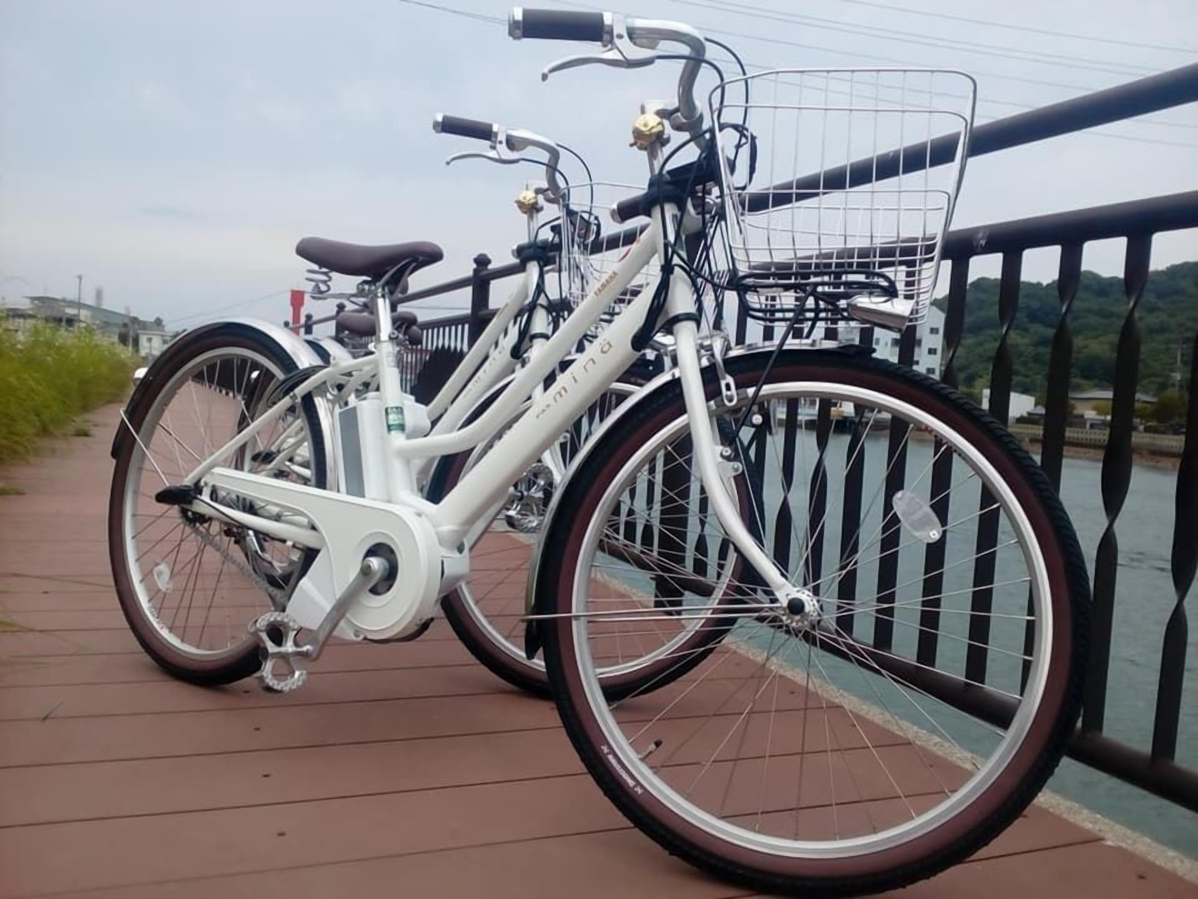 A white bicycle with a basket and a seat, parked on a bridge with a railing.