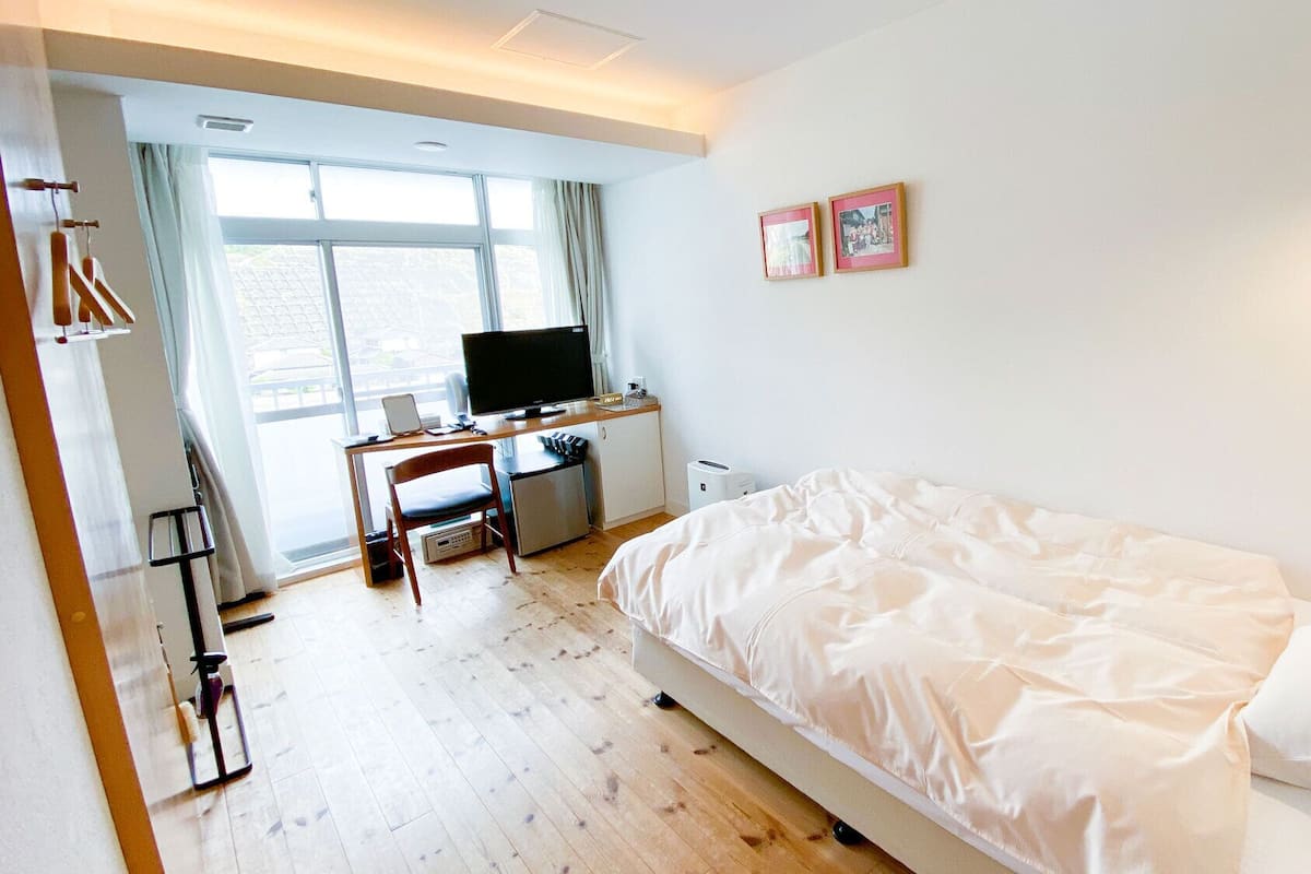 Une chambre à coucher avec un lit, un bureau avec un ordinateur, une télévision et une fenêtre.
