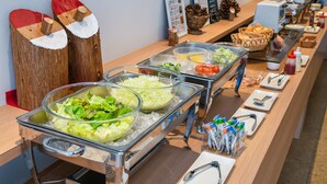 Buffet com diversas opções de comida, incluindo saladas e pão, disposto em uma mesa comprida com acabamento em madeira.