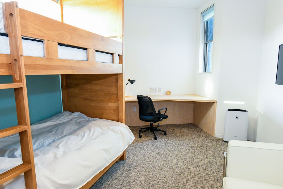 A bunk bed room with a desk and chair, a radiator, and a window.