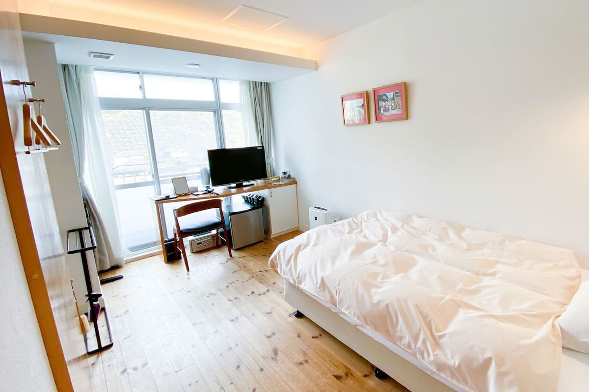 Une chambre à coucher avec un lit, un bureau avec un ordinateur, une télévision et une fenêtre.