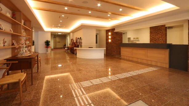 Um hall de hotel com balcão de recepção, estantes de madeira com objetos decorativos, área de estar com cadeiras e piso de mármore polido.