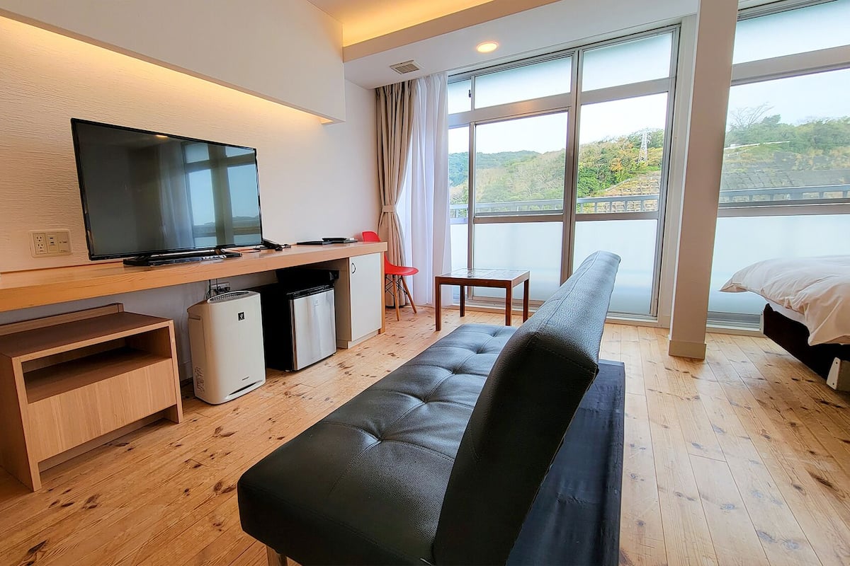 Una habitación de hotel moderna con televisión de pantalla plana, un sofá, una mesita y una ventana con vistas al exterior.