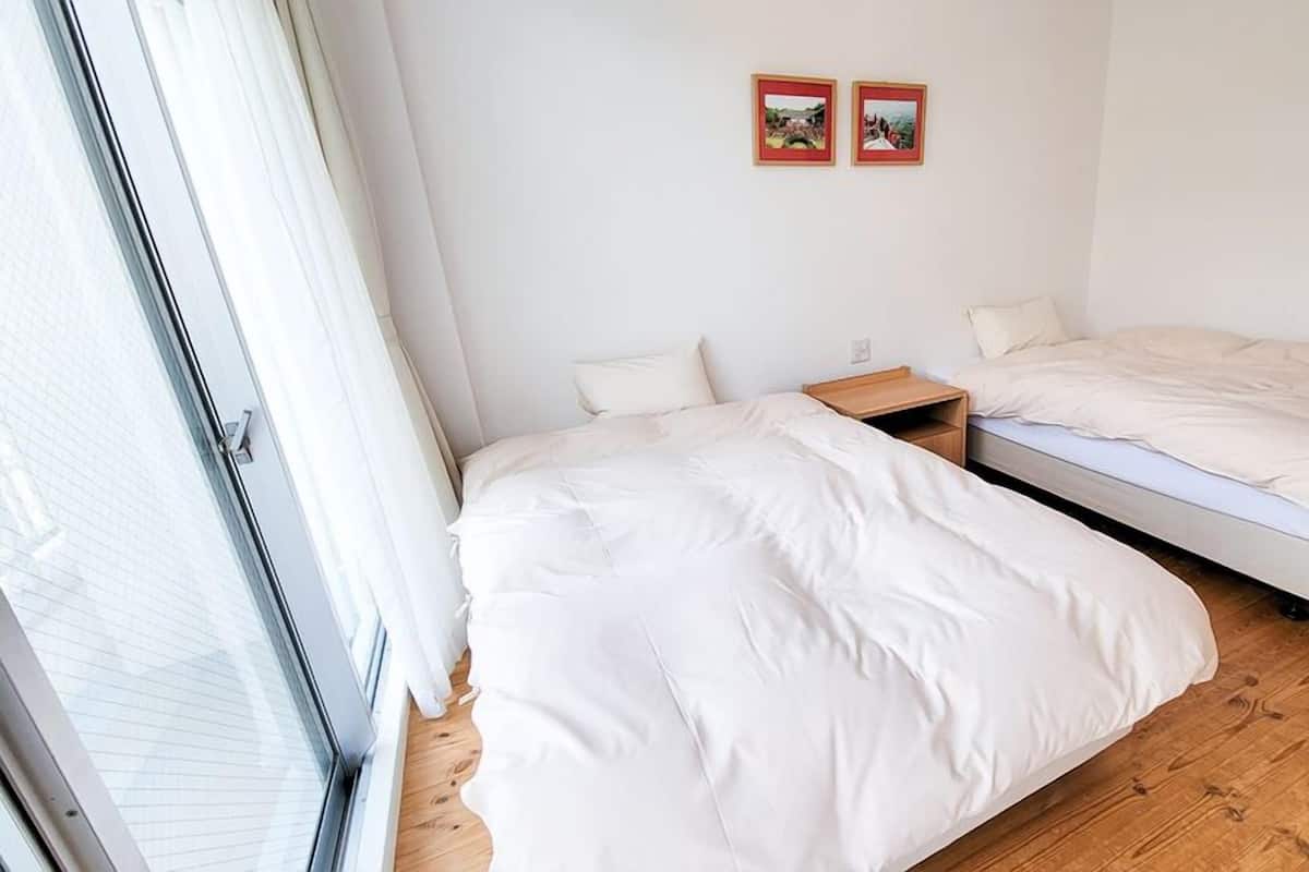 Une chambre avec deux lits, un plancher en bois et une fenêtre avec des stores.
