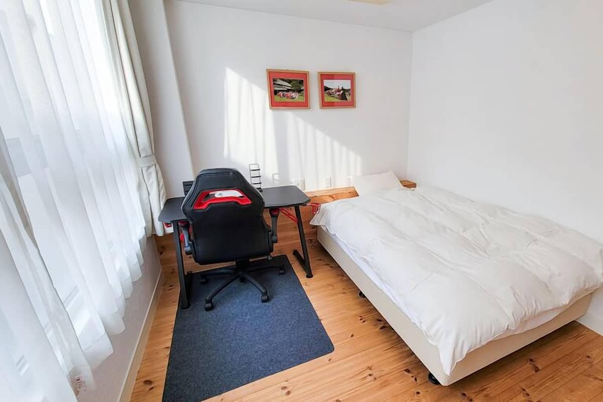 Une petite pièce propre, avec un lit simple, un bureau et une chaise, et deux tableaux encadrés accrochés au mur.