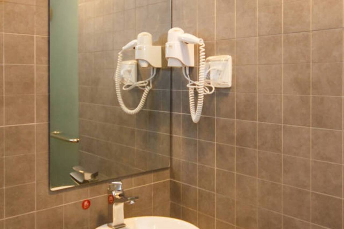 A bathroom with a large mirror, a sink, and two hair dryers mounted on the wall.