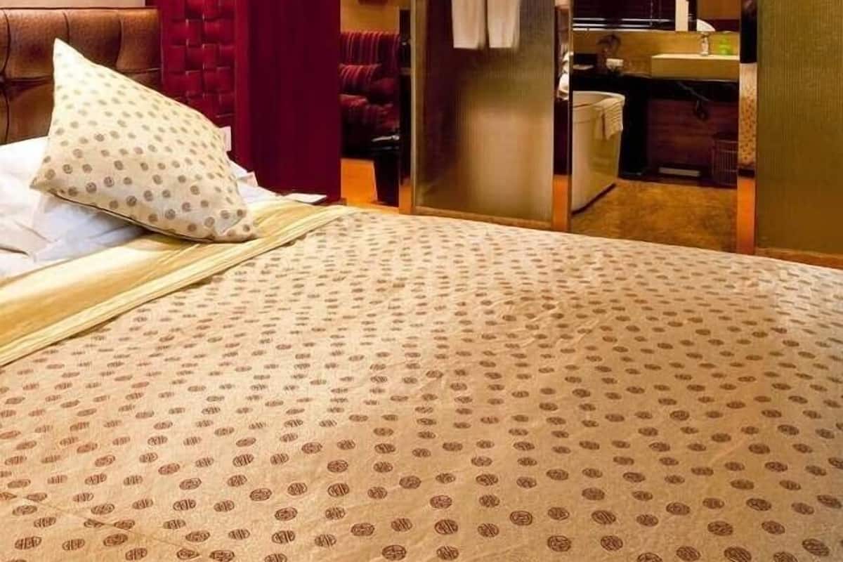 Quarto de hotel com cama, parede de destaque vermelha, banheiro com espelho e área de chuveiro.