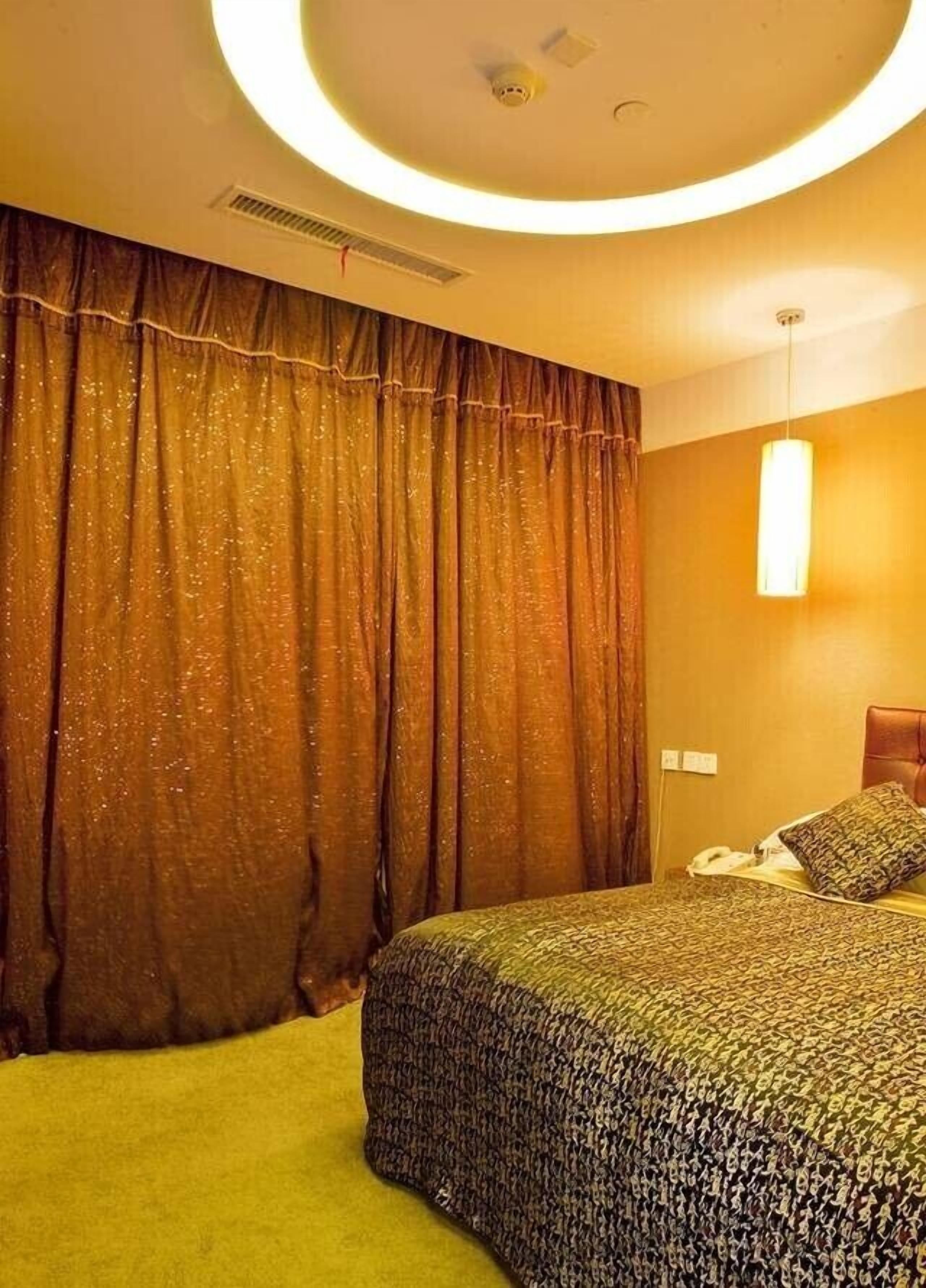 A hotel room with a large bed, a curtain, a wall-mounted light, and a ceiling vent.