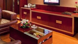 A hotel room with a leather sofa, a small coffee table with a vase of flowers, a minibar, and a television mounted on the wall. - Tieliu Business Hotel (Hangzhou)