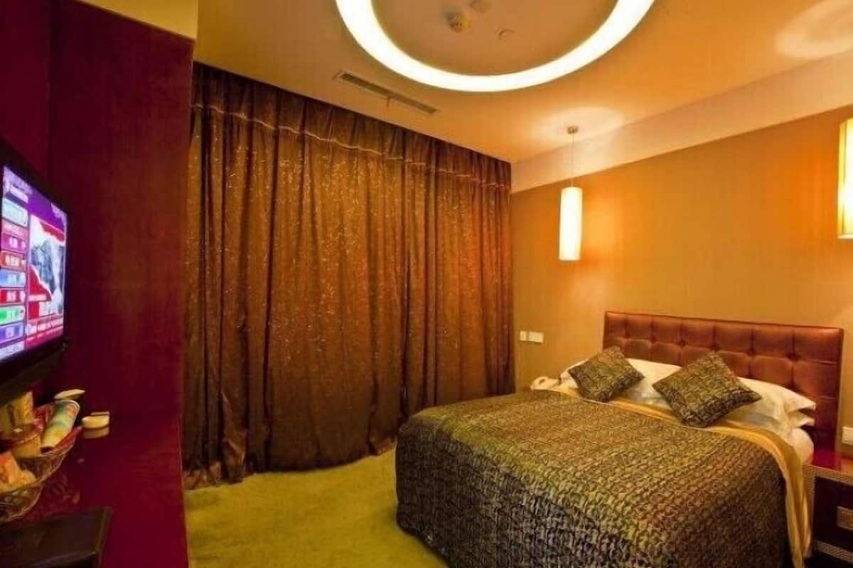 Quarto de hotel com uma cama grande, televisão à esquerda e luminária circular no teto.