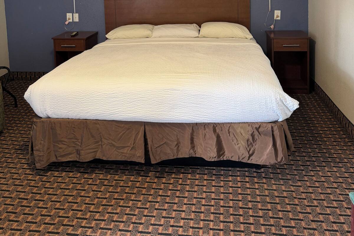 A hotel room with a large bed, two bedside tables with lamps, a framed picture on the wall, and a patterned carpet.