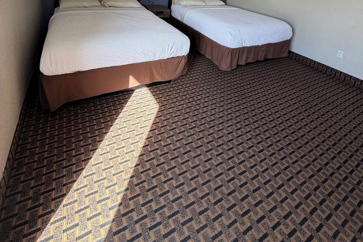 A hotel room with two beds, a patterned carpet, and framed pictures on the walls.