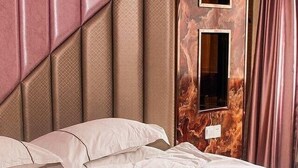 A neatly made bed with a headboard featuring a geometric pattern, a wall-mounted mirror, and a window with curtains. - Chaolv Business Hotel (Hangzhou)
