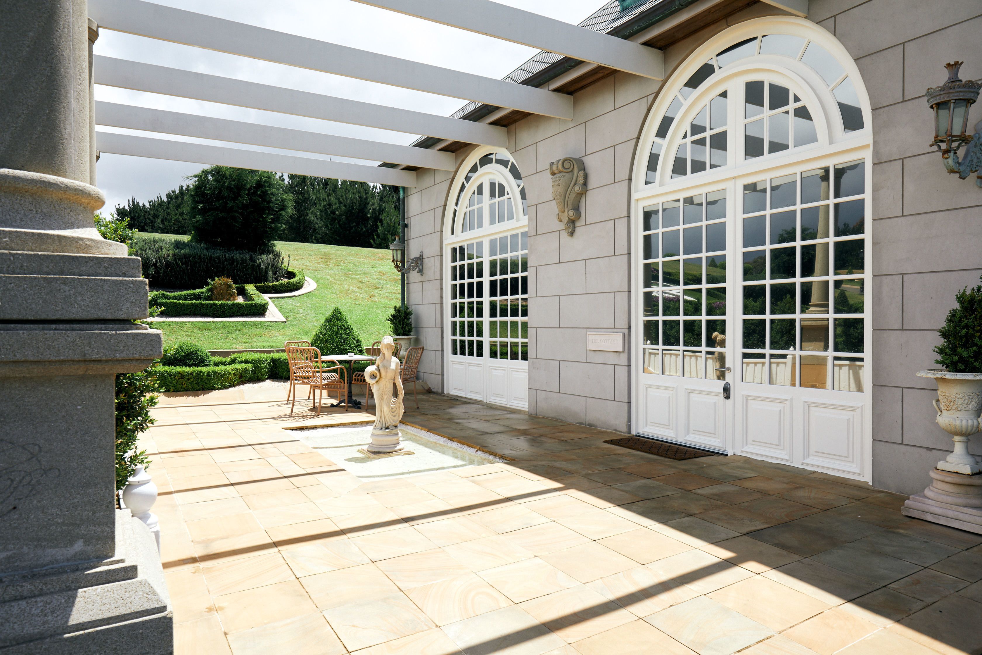 A covered patio with stone flooring, a statue, and a view of a well-manicured lawn.