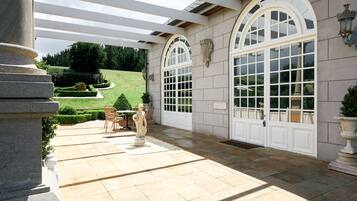 A covered patio with stone flooring, a statue, and a view of a well-manicured lawn.