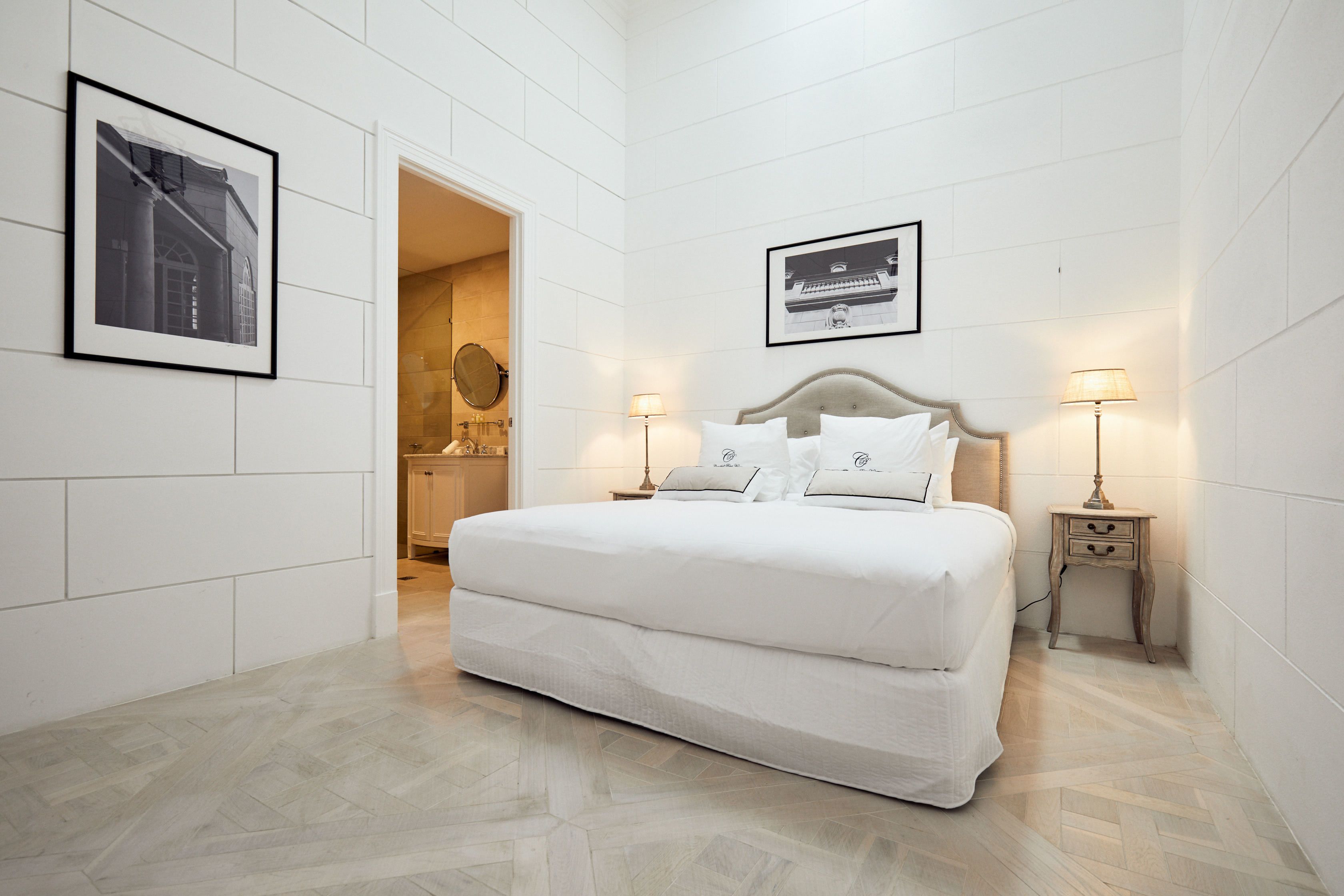 A hotel room with a large bed, two bedside tables with lamps, a framed picture on the wall, and a door leading to a bathroom.