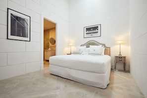 Ein Hotelzimmer mit einem großen Bett, zwei Nachttischen mit Lampen, einem gerahmten Bild an der Wand und einer Tür zu einem Badezimmer.