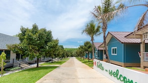 A pathway lined with palm trees and houses with a 'hello and welcome' sign. - Be Leaf Resort (Thep Krasattri)